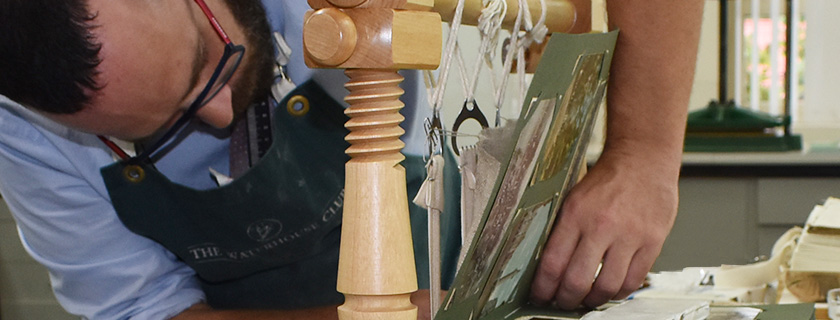 Conservator hand sewing pages of a postcard album to tapes 